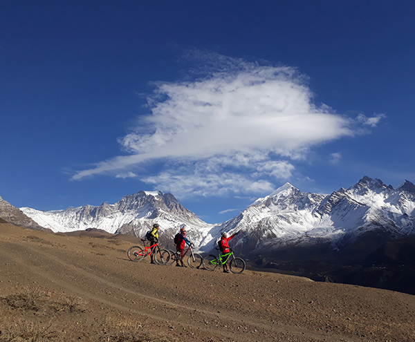 Three mountain bikers riding the single track of Mustang and the view of Himalayan range seen on the background.
