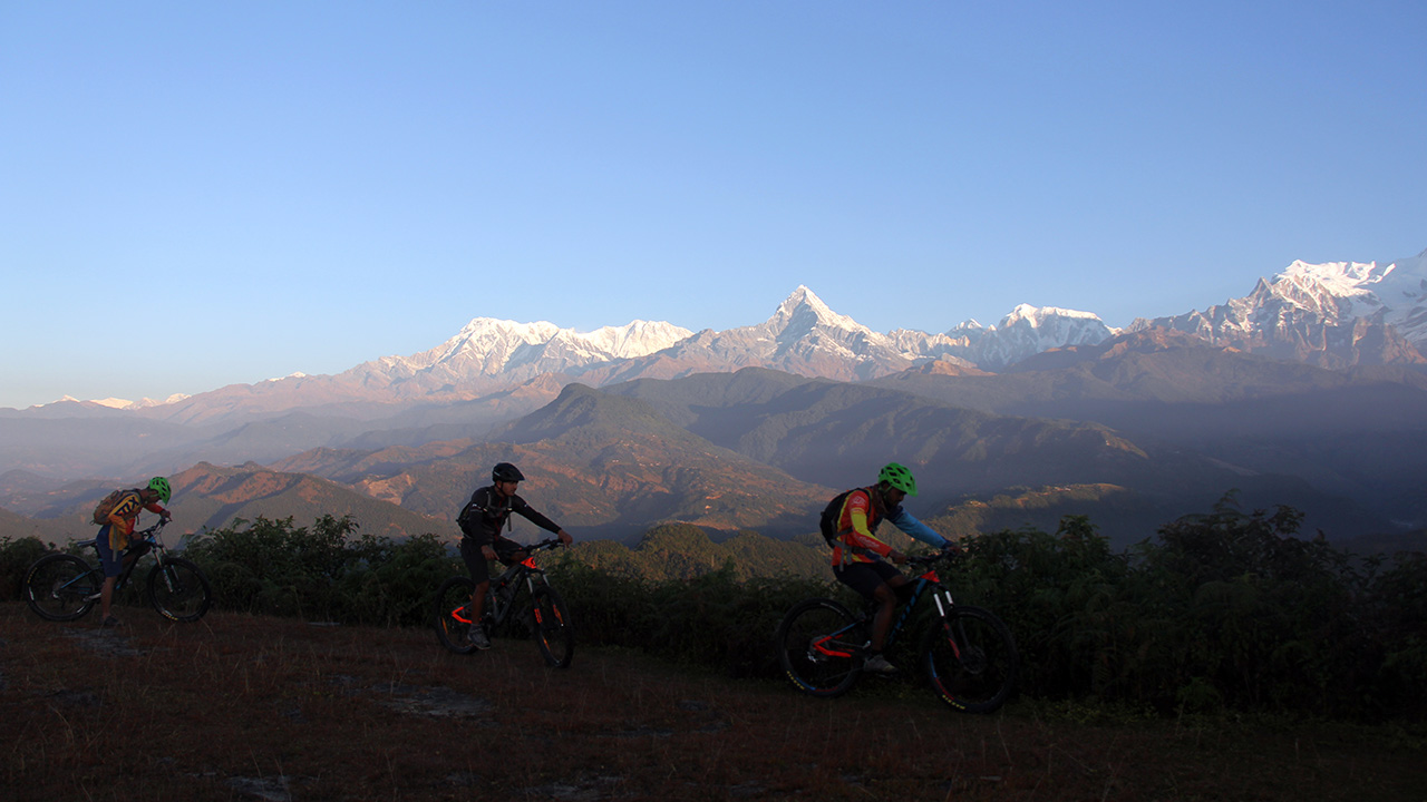 Three mountain bikers enjoying their ride with the view of Dhaulagiri, Annapurna I, Fishtail and Annapurna III starting from left.