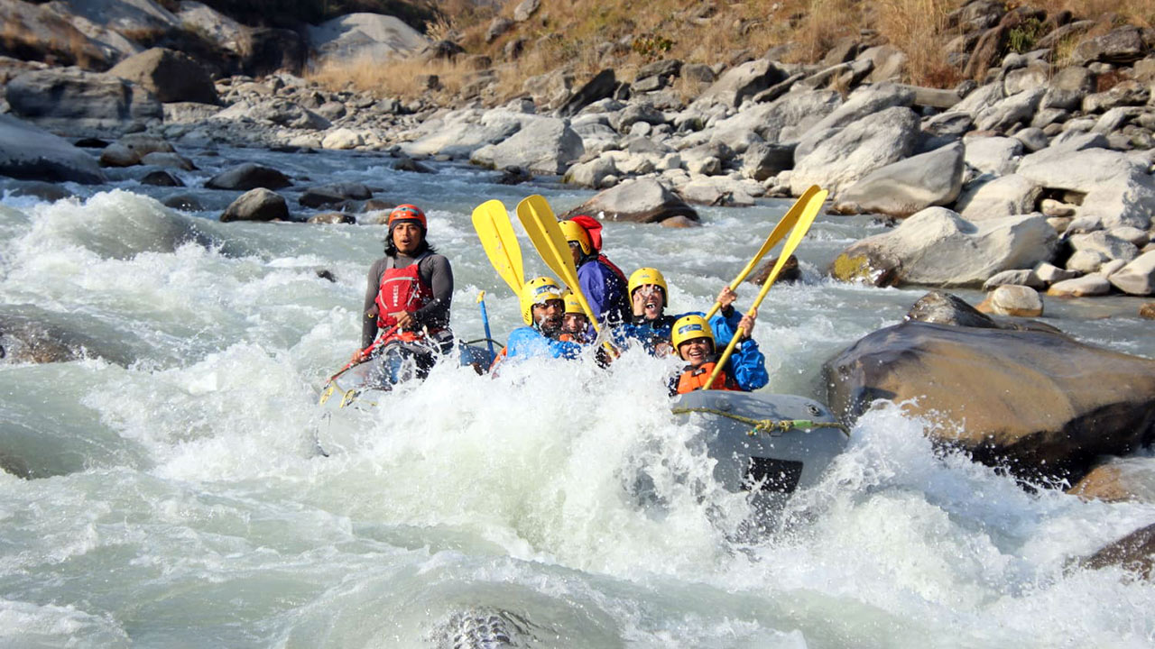 A group of people on the raft are cheering the white water rafting with their paddle raised in the air.