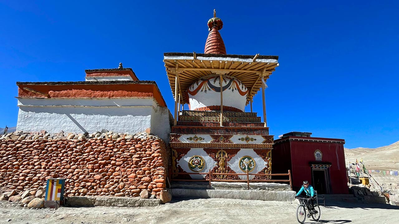 A mountain biker traverses by the side of Monasteries on the sides and a Chhorten painted red and white and carved with Tibetan scriptures in the middle, in upper mustang.