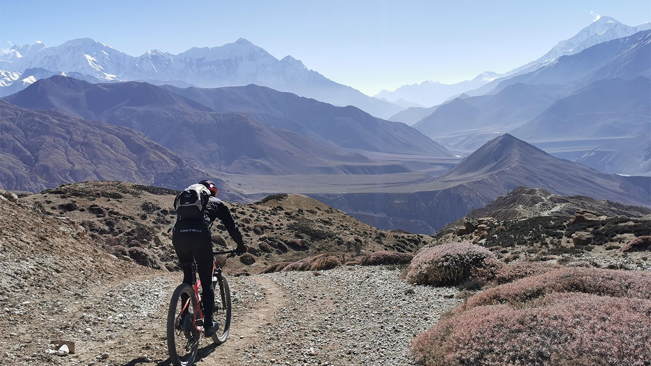 A mountain biker in Black outfit enjoys his ride along the single track of Mustang with the views of Dhaulagir, Nilgiri and tilicho peak.