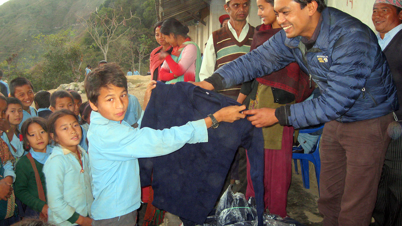 A man in blue jacket is distributing winter sweater among the under privileged children at a school in Kutumsa, Syangja. 