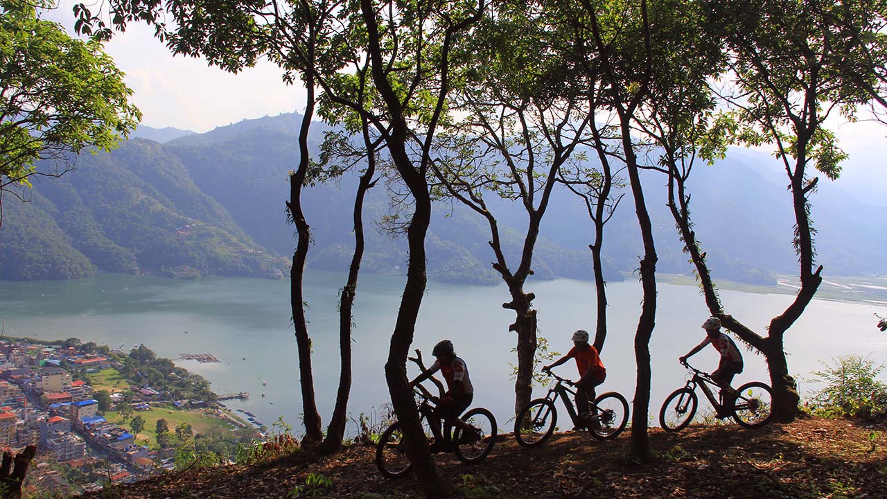 E-MTB riders riding through the forest to Sarangkot with the view of Fewa Lake and Raniban.