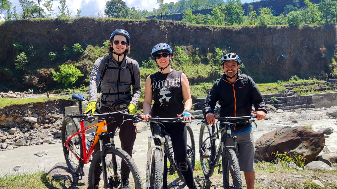 Three mountain bikers are posing for a picture with smiles on their face at the bank of Seti River.
