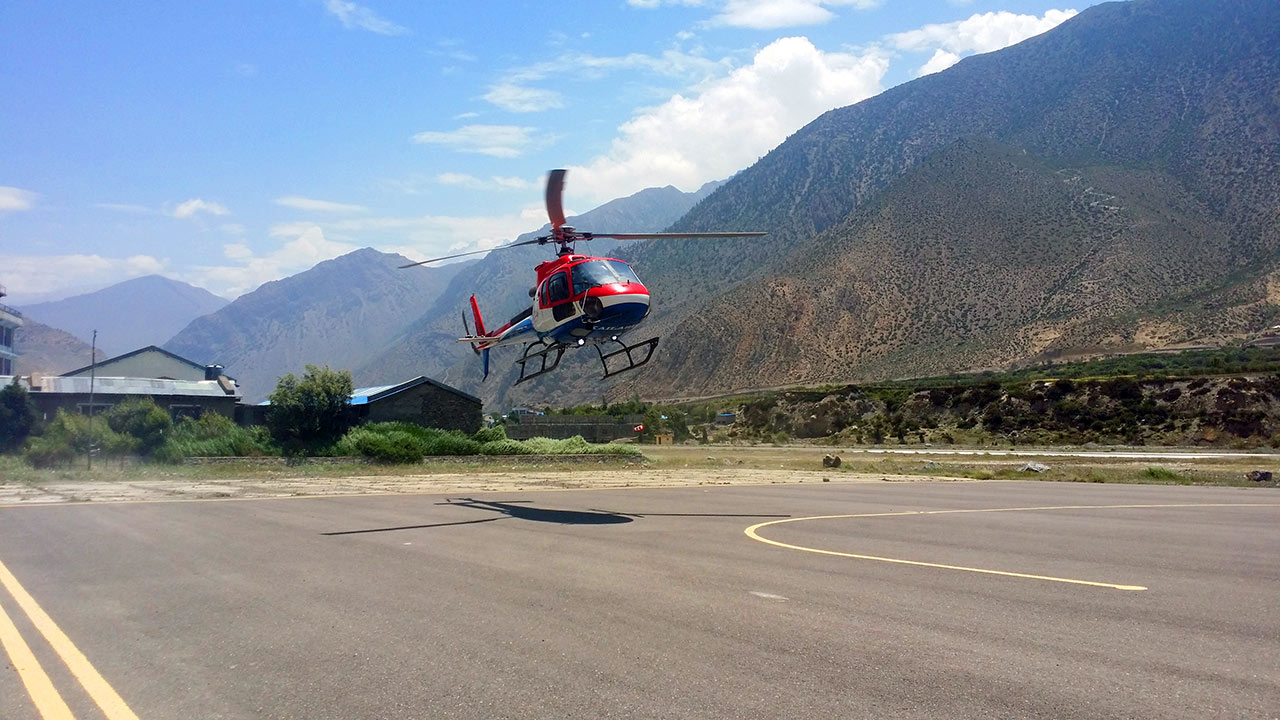 A Heli-Copter in red, blue and white is taking off to head to Muktinath and Thoron-La from Jomsom airport in Mustang.