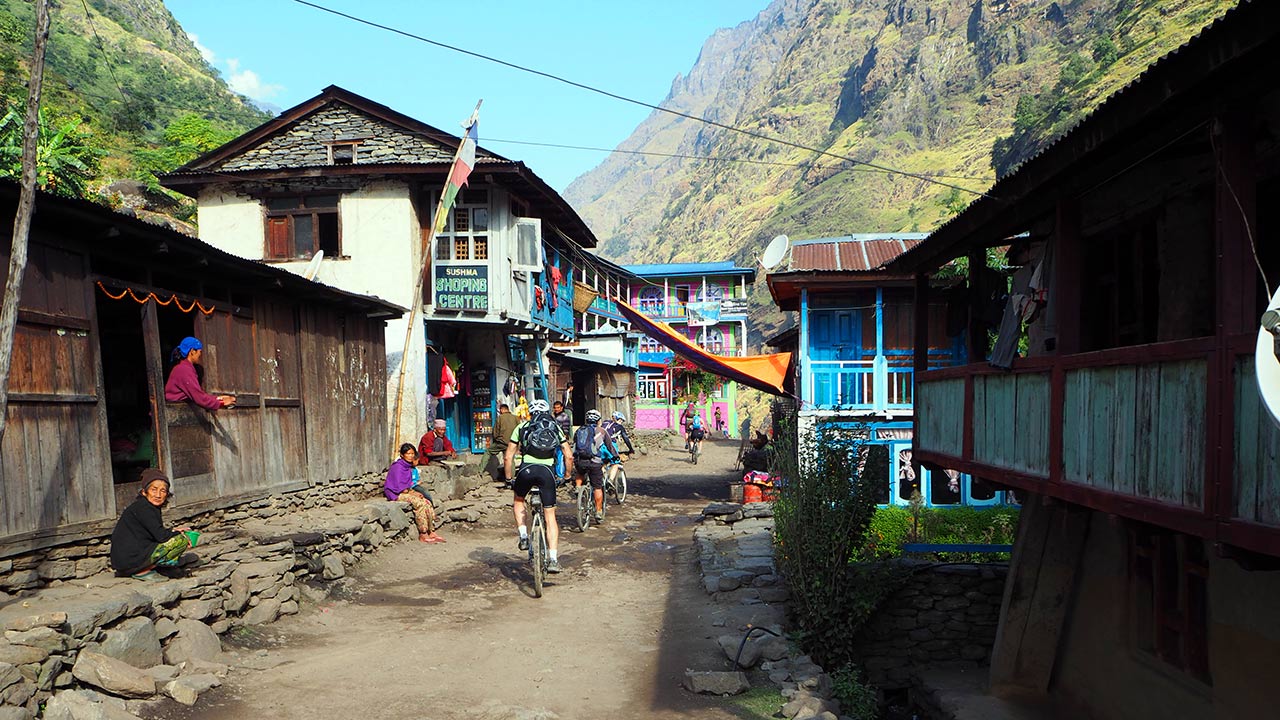 A group of mountain bikers on their mountain bikes on the way to Manang, passing through the colorful village of Jagat while greeting Namaste to friendly locals.