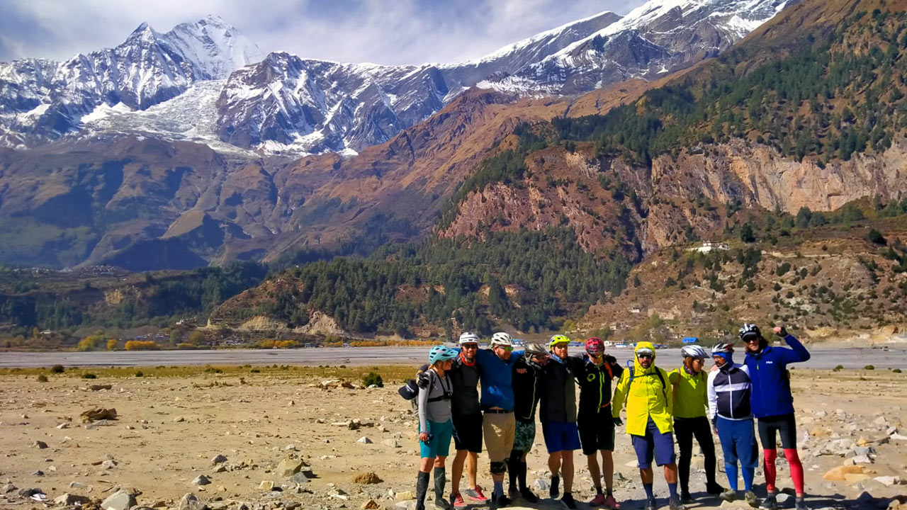 A group of mountain bikers are keeping their hands on each others' shoulder to cherish the moment and to take a beautiful picture on the Kaligandaki river-bed with the view of Dhaulagiri on the background.