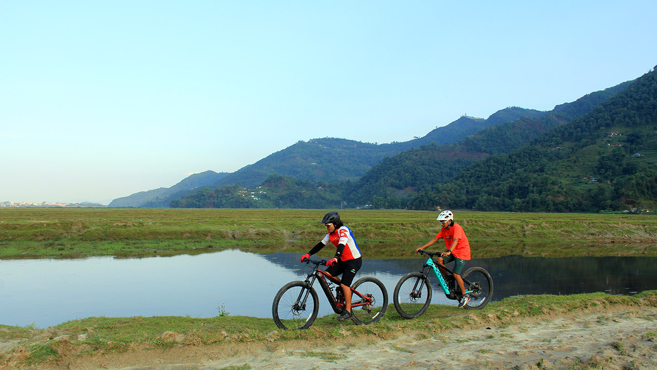 Two mountain bikers on their Electric mountain bike are riding along the river dyke in Pokhara, Nepal.