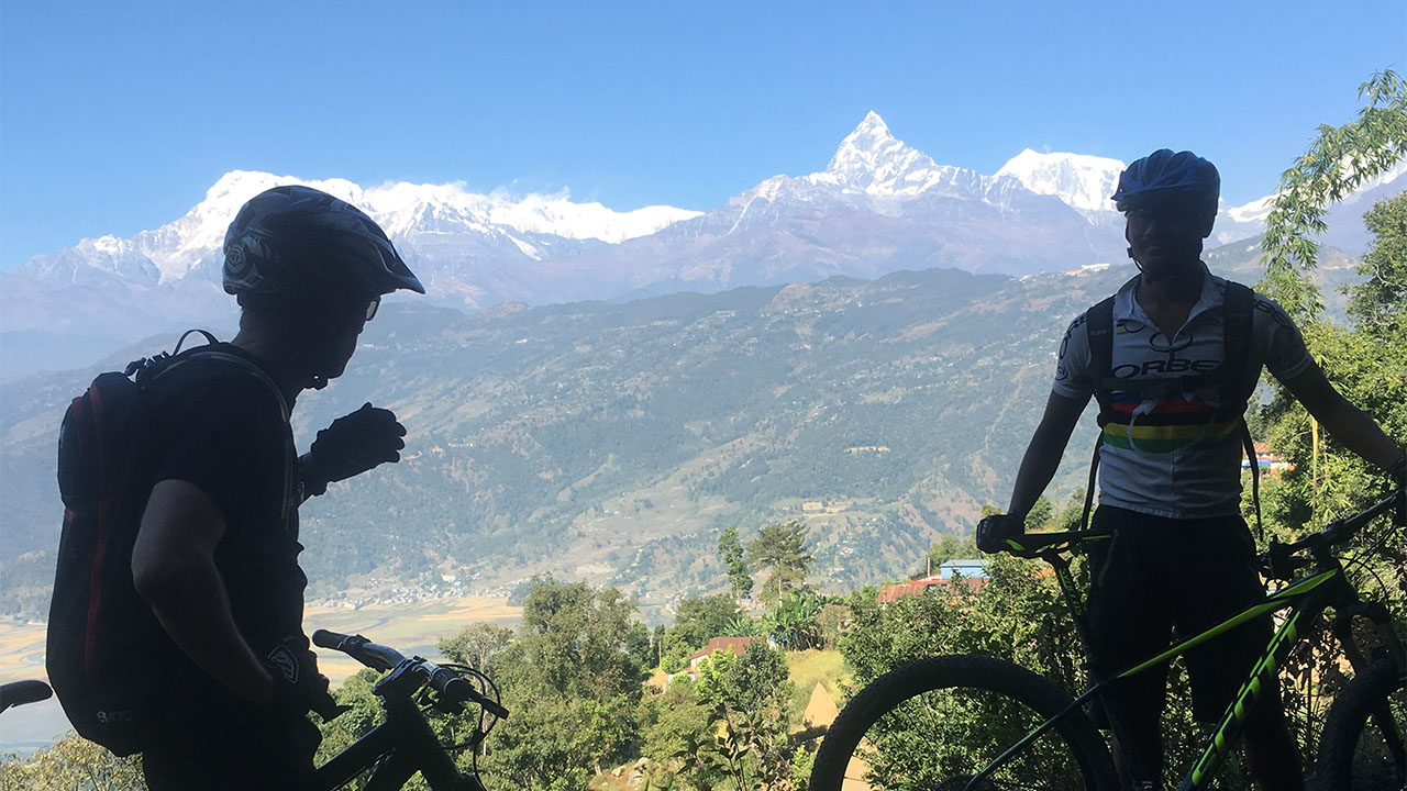A mountain biking guide telling the name of the Himalayas to his client
