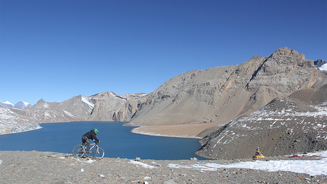 A biker in green helmet is riding his bike on the bank of Tilicho Lake in Manang, Nepal.