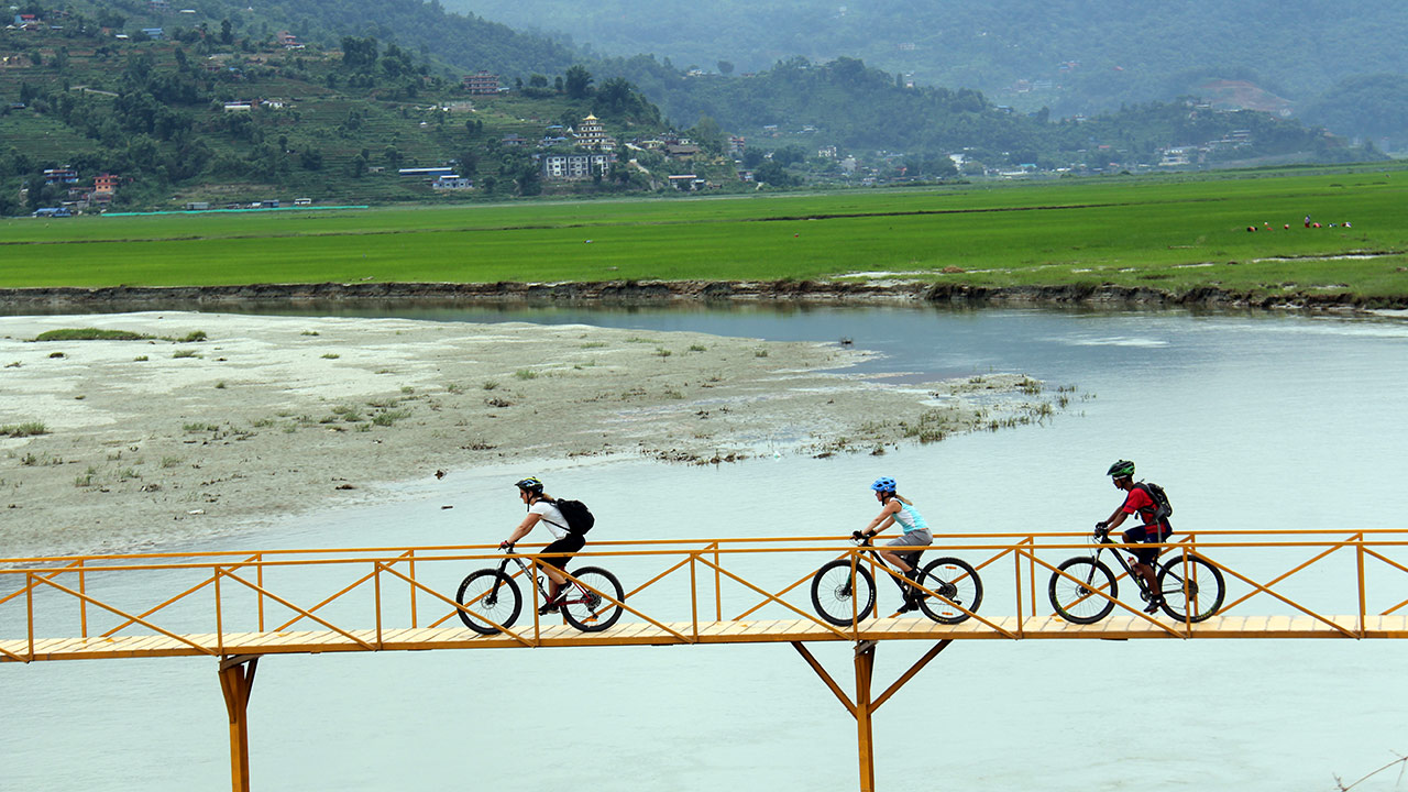 Three mountain bikers are biking through the yellow bridge over Harpan River in Pame village.