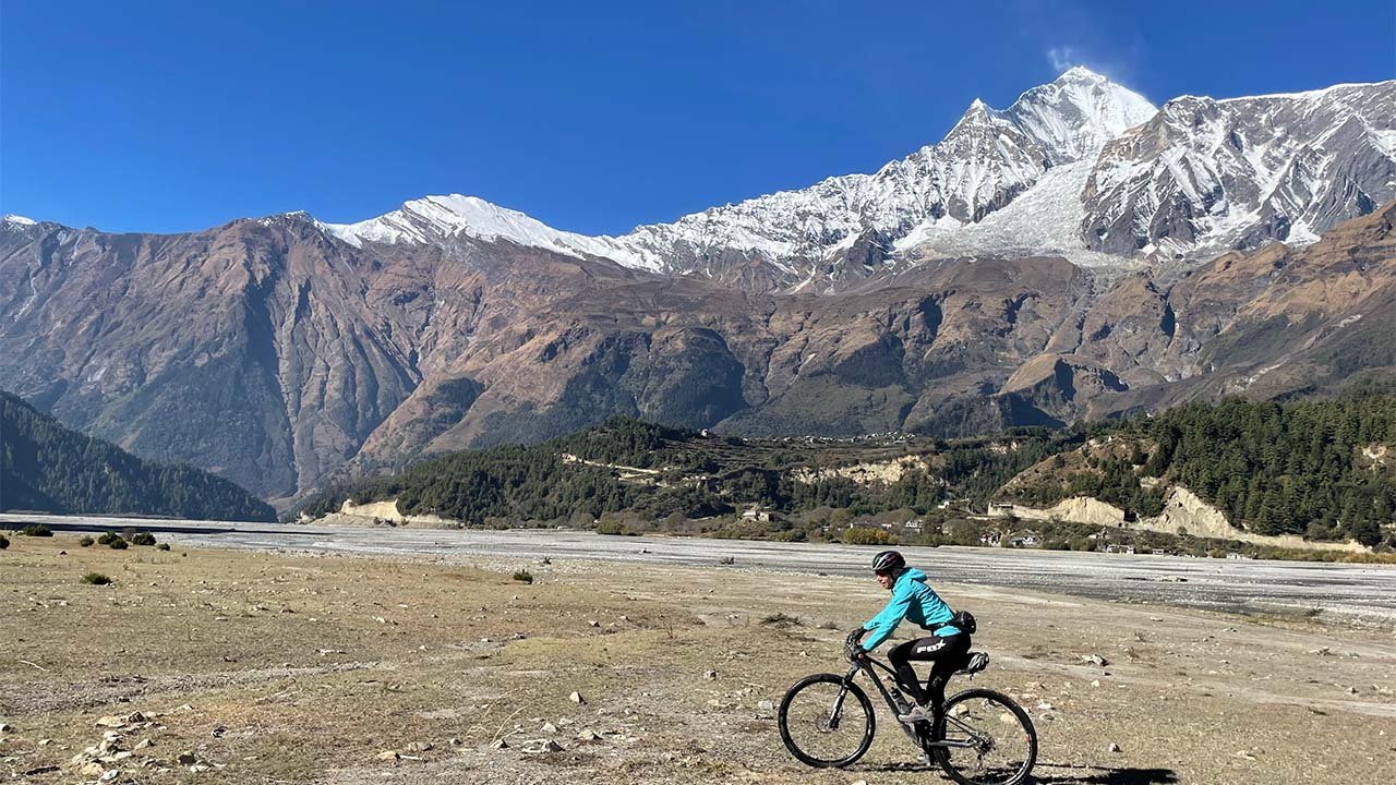 A biker in blue jacket rides his mtb on the Kaligandaki River bed with the back-drop of Dhaulagiri.
