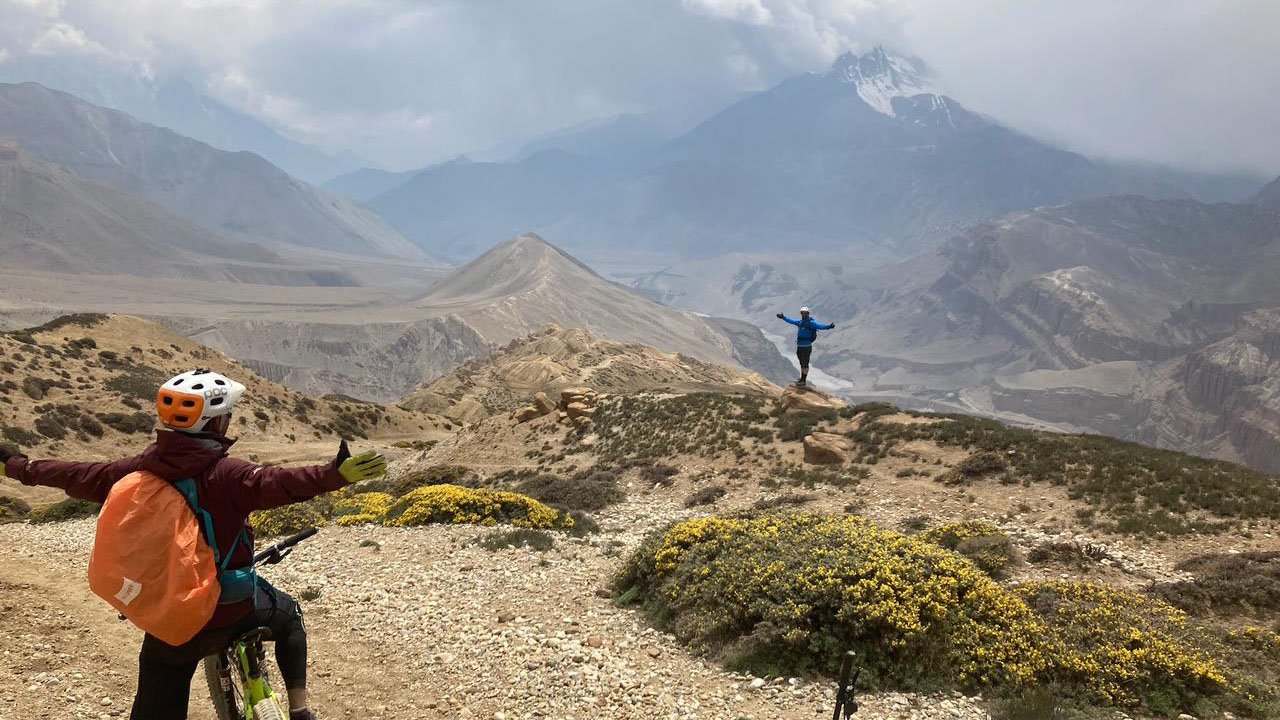 Two mountain bikers are cheering each other raising their hands side ways in the air during their Upper Mustang mountain bike tour.