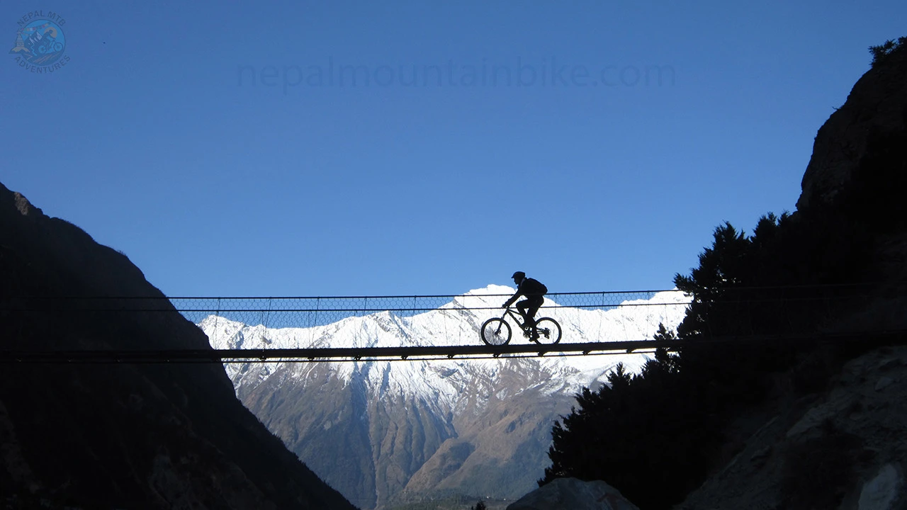 A MTB rider rides over the bridge in Lower Mustang during Nepal's top Himalayan cycling adventure.