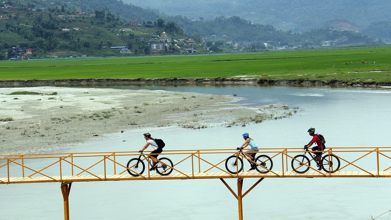 Mountain bikers are crossing the yellow bridge over Harpan River near Pame village.