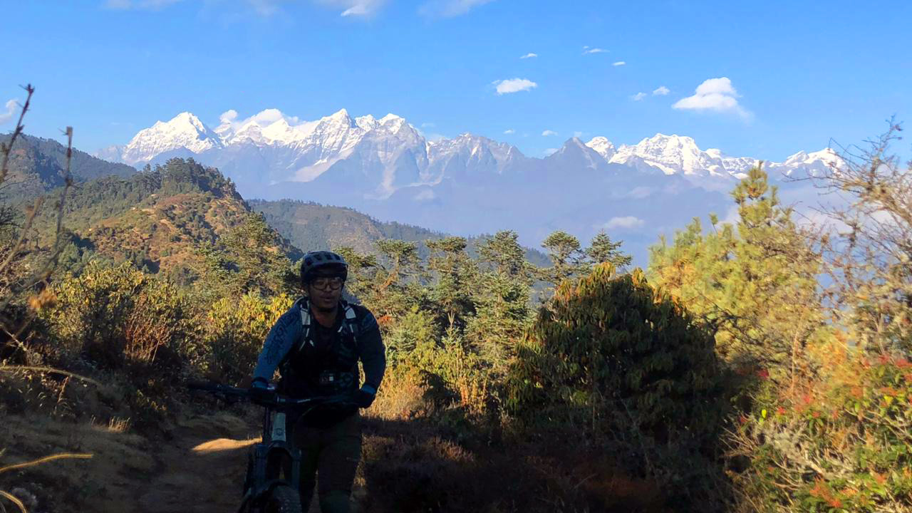 A mountain biker with black helmet is pushing his mountain bike with the backdrop of Peaky Peak.