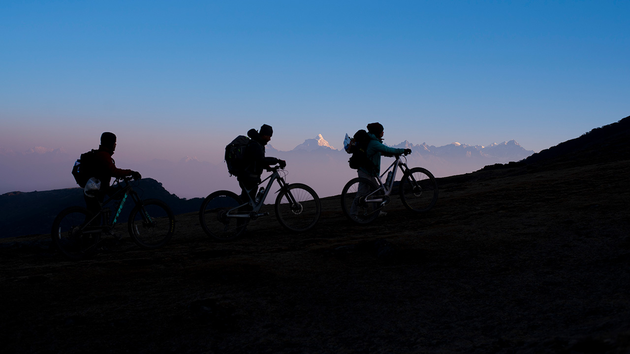 A group of three bikers are pushing their bikes to the summit of Pikey Peak in the Everest Himalayan region.