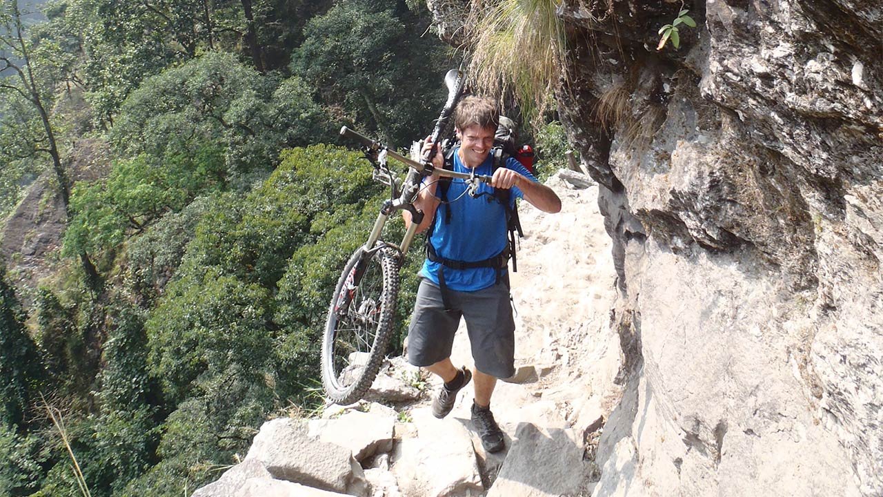 A man in his blue top is carrying his mountain bike during his tour to Manaslu Circuit.