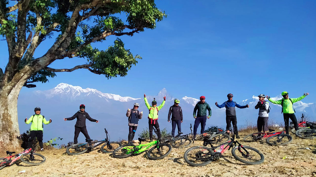 Mountain bikers are posing for a picture with their bikes laid on the ground along with the beautiful view of Annapurna and Fishtail mountain at Pumdikot Shiva Temple.