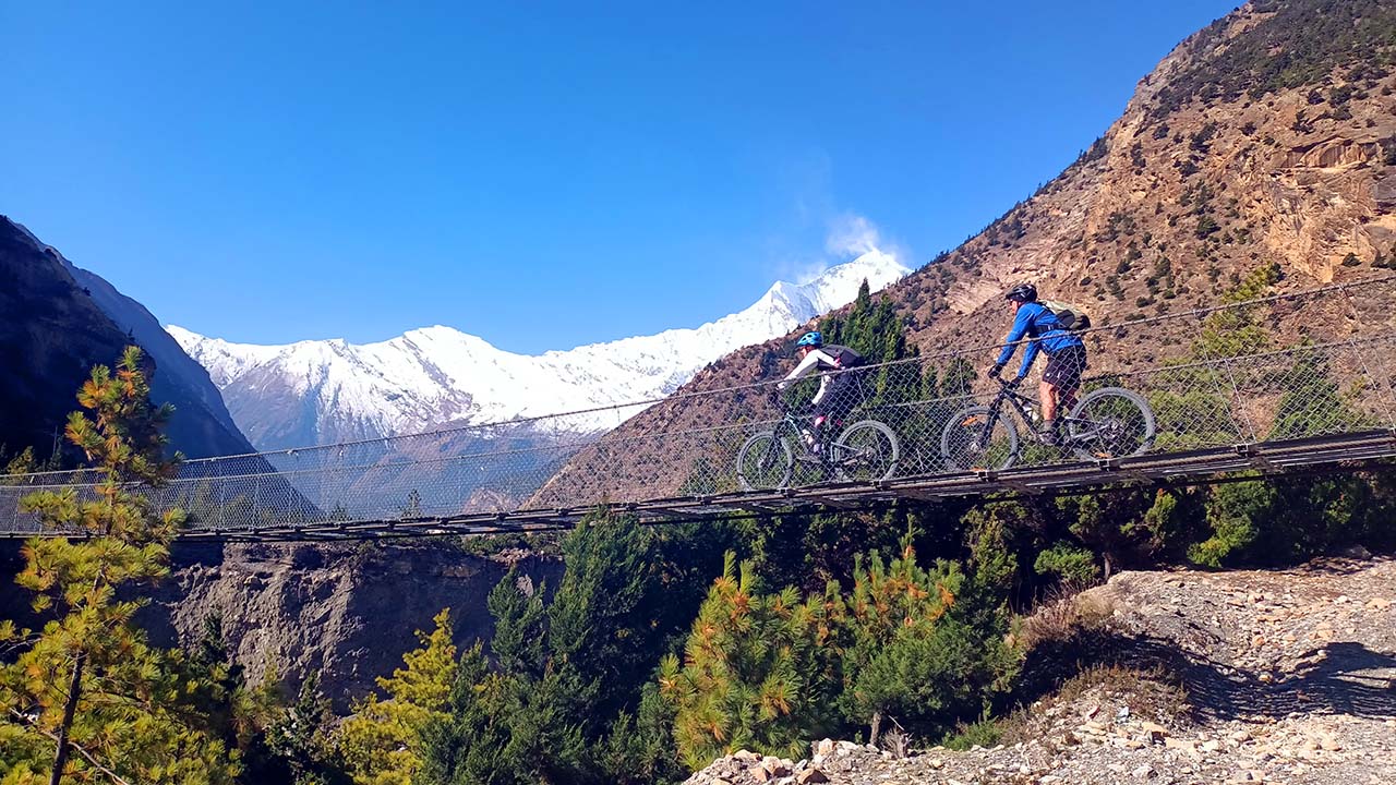 Mountain bikers are crossing the suspension bridge in Tukuche during their mountain bike tour in Mustang.