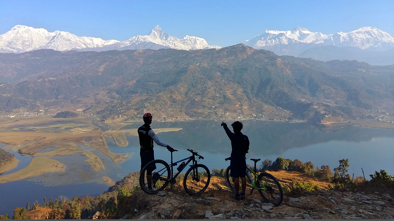 A MTB Guide is telling the name and altitude of the Annapurna and Fishtail mountains in their tour to round the Fewa Lake.