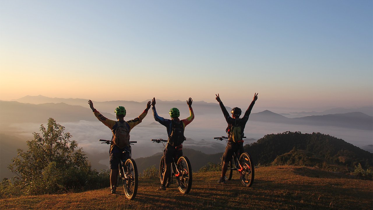 Three mountain bikers are cheering the beautiful view raising their hands in the air.