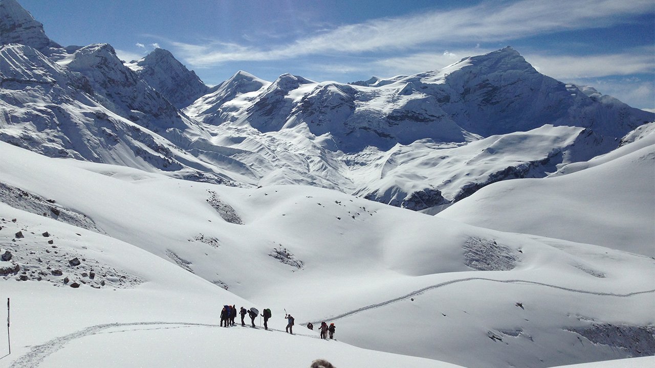 A group of trekkers ascending towards thorong-la pass on a snow-covered track in Annapurna Circuit trek.