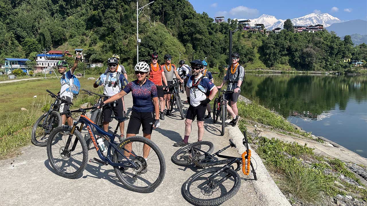 Group of mountain bikers with their bikes are posing for the picture at Begnas Lake, with the stunning view of Annapurna and Begnas Lake.