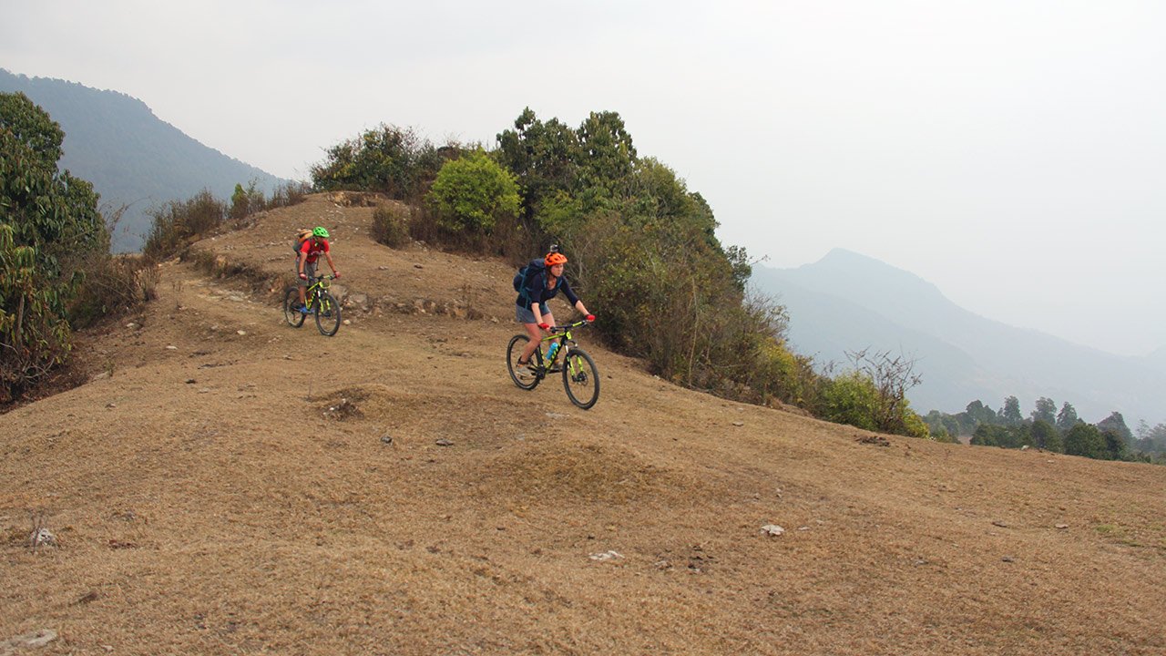 Mountain bikers, the front one with a orange colored helmet and the back one with green are enjoying their ride in the beautiful landscapes of Panchase.