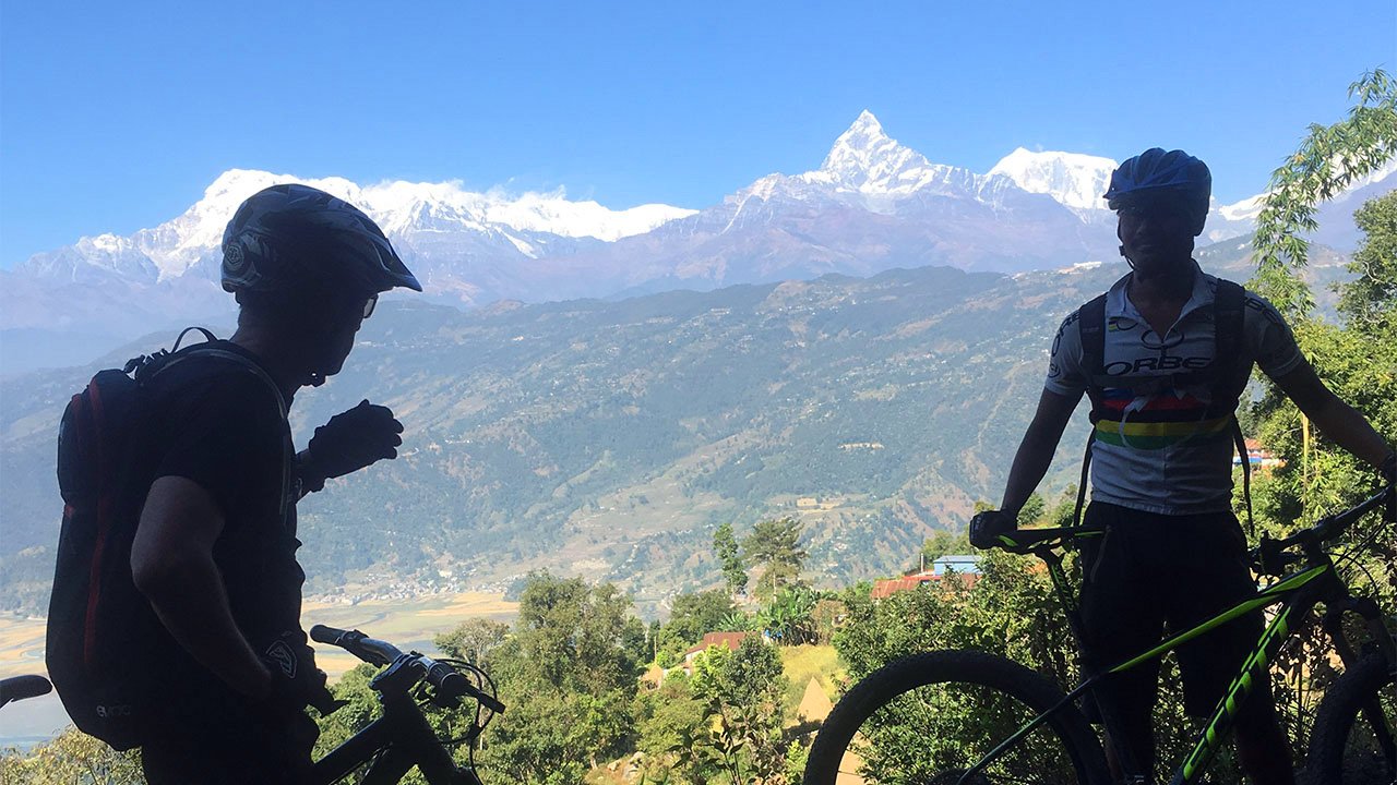 A mountain bike guide is explaining the names of the Annapurna mountain range to his client on the way to Stupa.